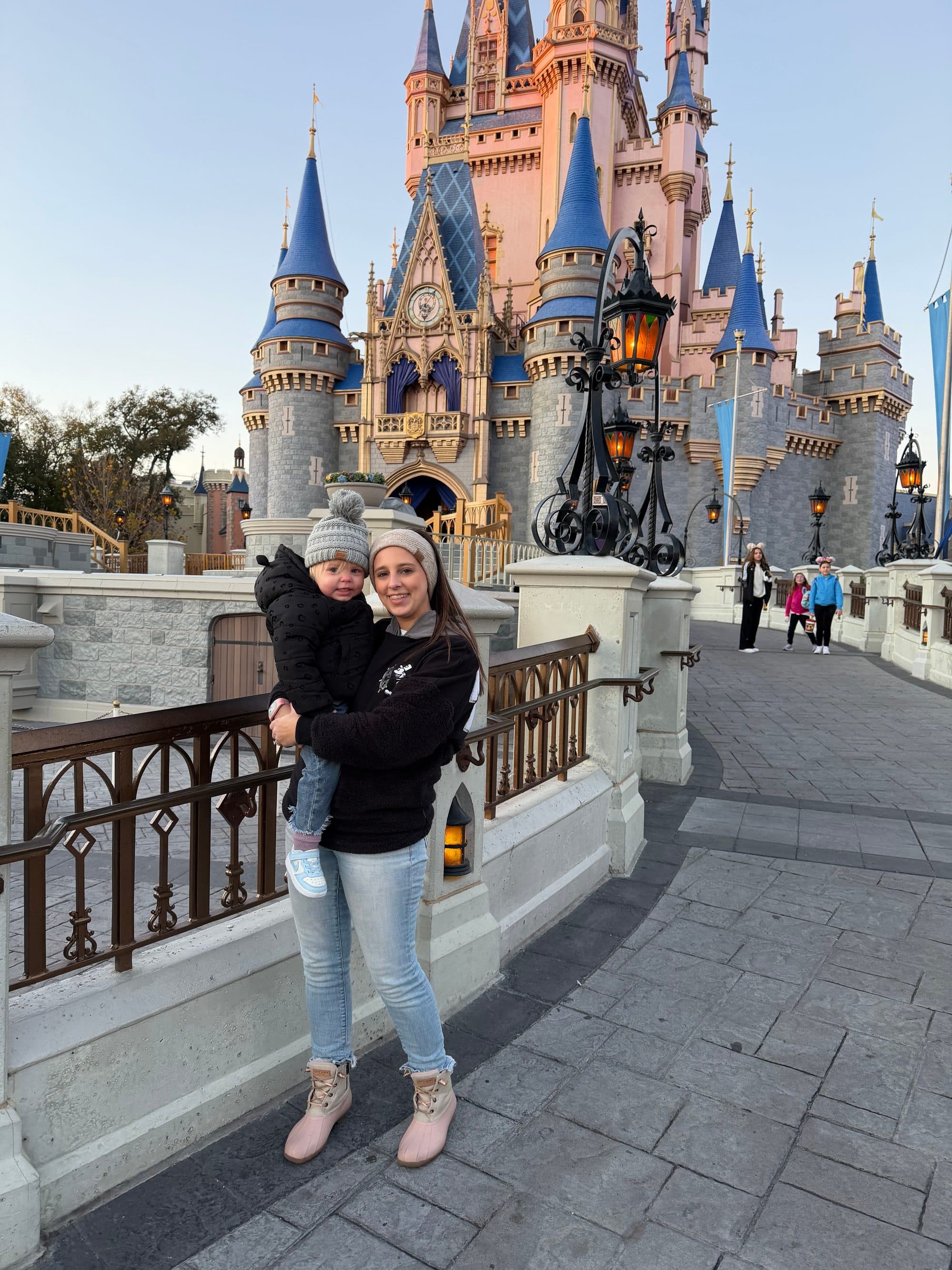 Mom holding a toddler in front of Cinderella Castle at sunset