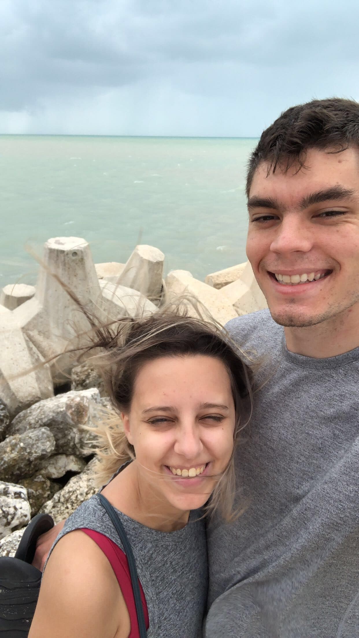 Couple taking a selfie on a breakwater with the ocean behind them