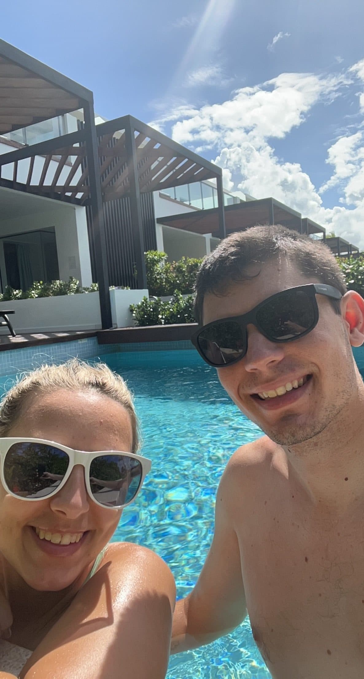 Couple taking a selfie in a resort pool with villas in the background