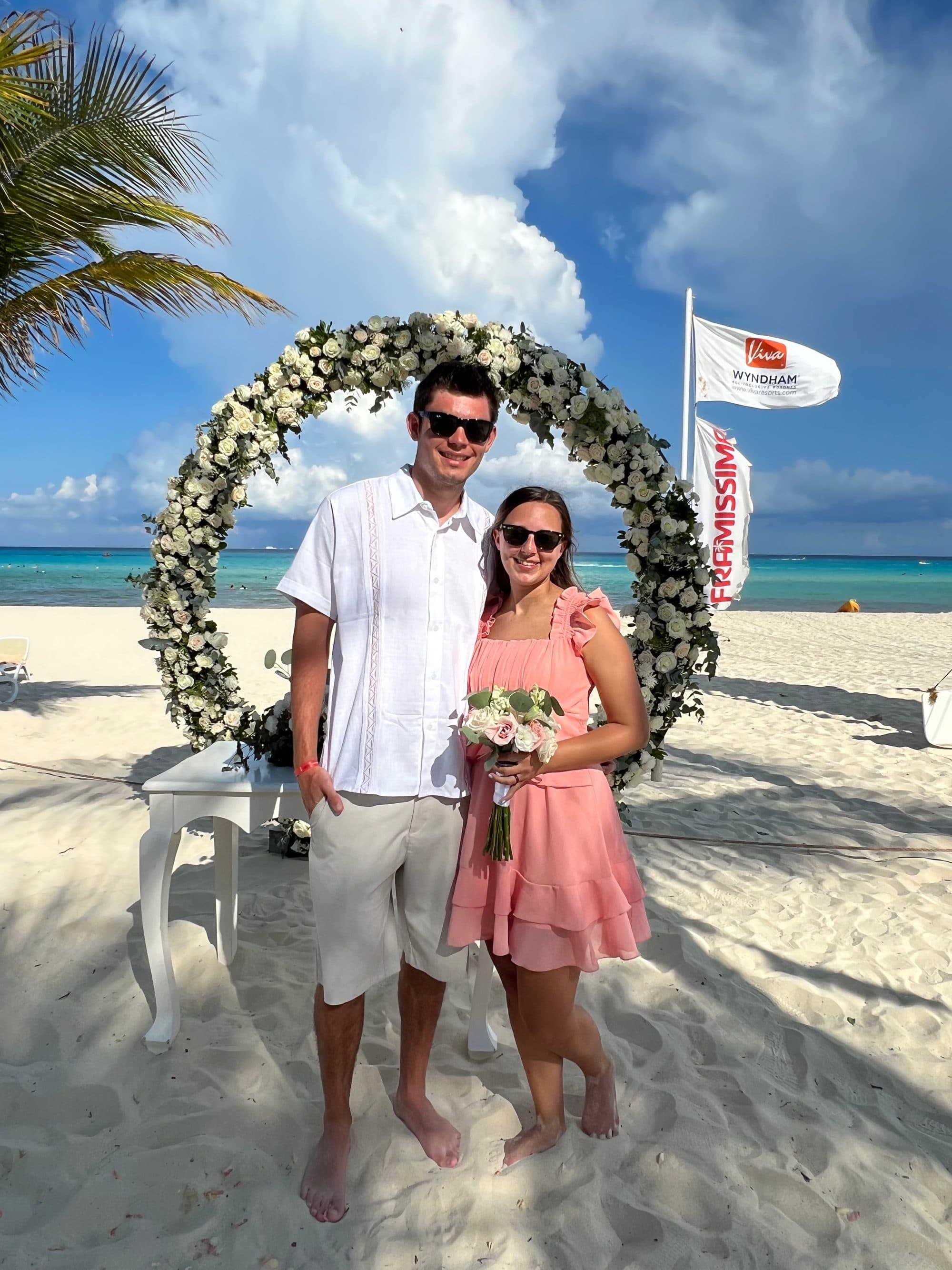 Couple standing under a beachfront floral wedding arch at an all-inclusive resort
