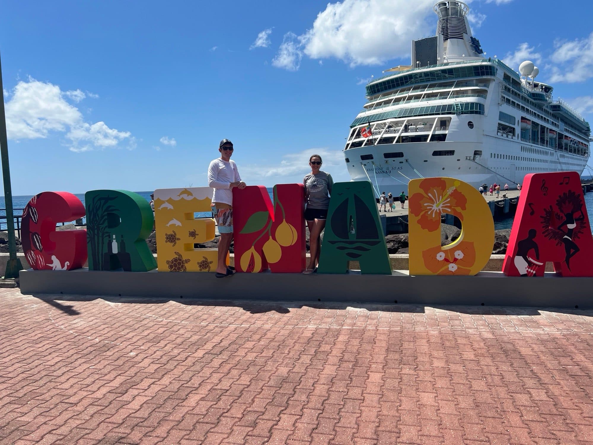 Brooke and her husband at the Grenada welcome sign with their cruise ship docked behind them