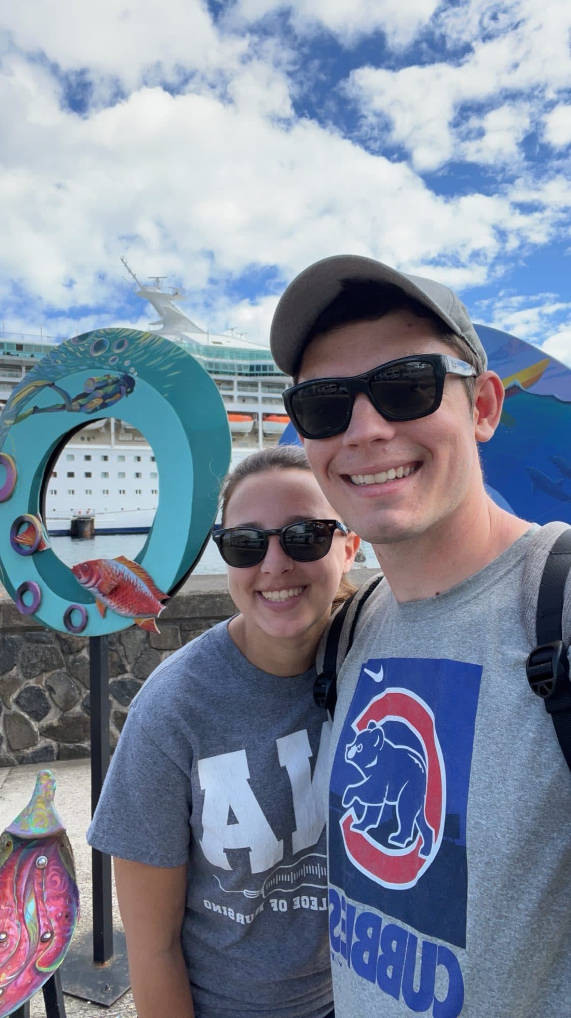 Brooke and her husband smiling in front of a cruise ship docked at port